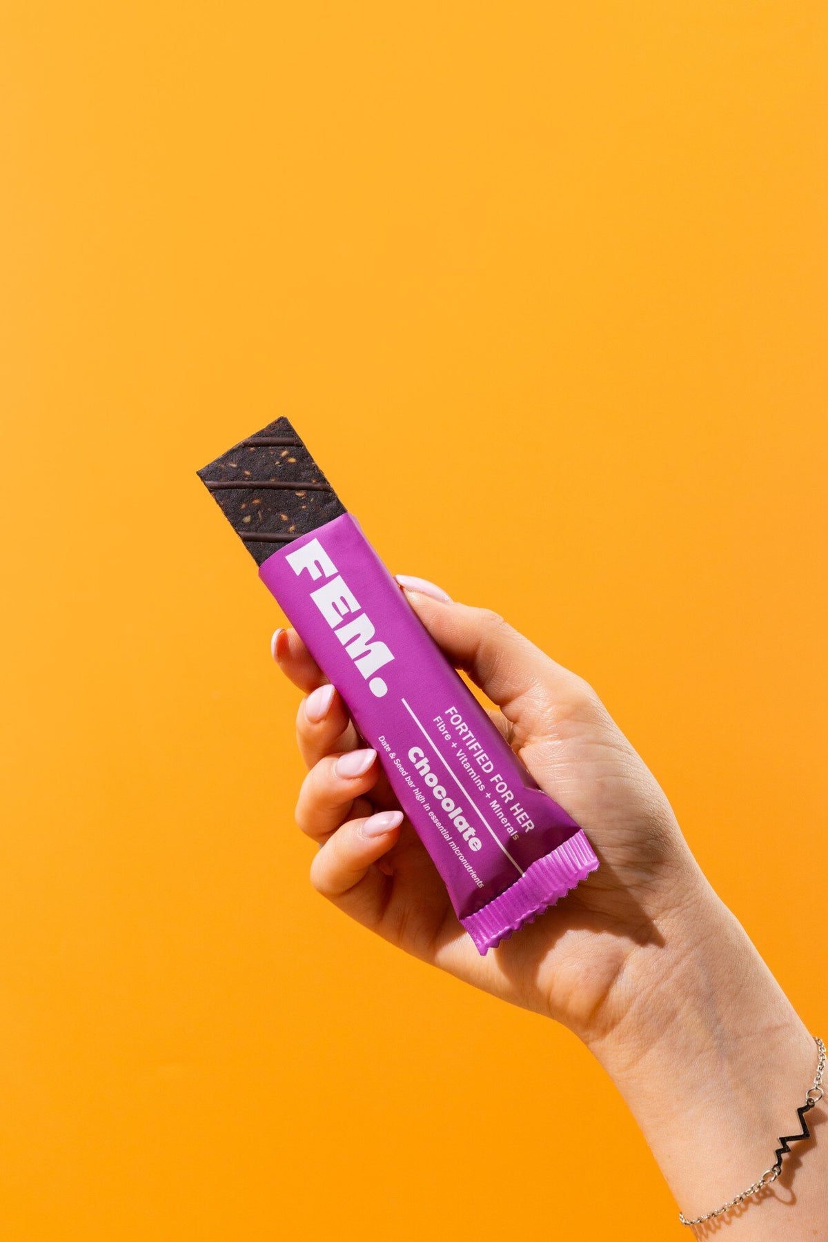 Hand holding an opened FEM. Chocolate bar against an orange background