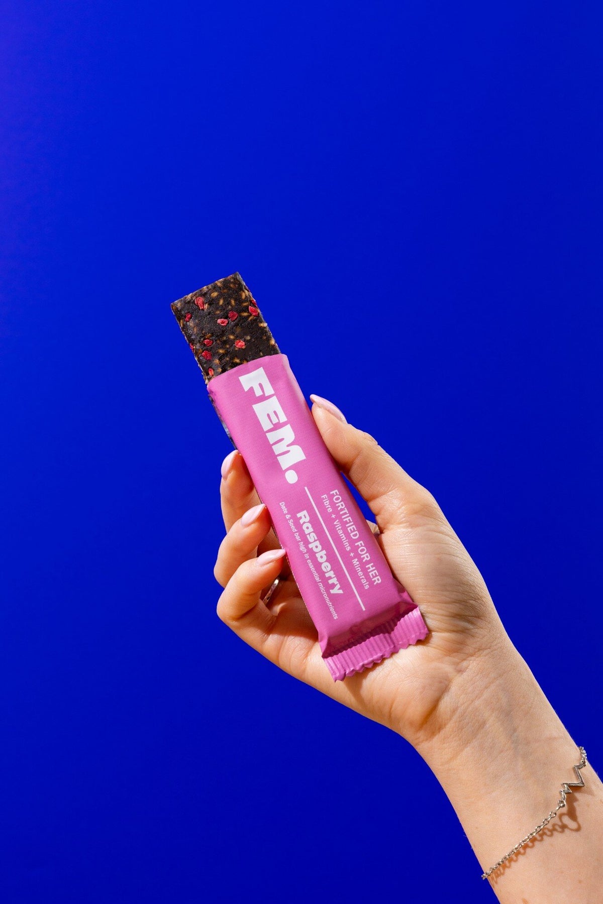 Hand holding an opened FEM. Raspberry bar against a blue background