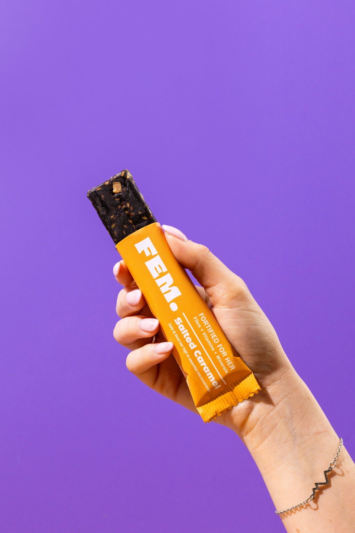 Hand holding an opened FEM. Salted Caramel bar against a purple background